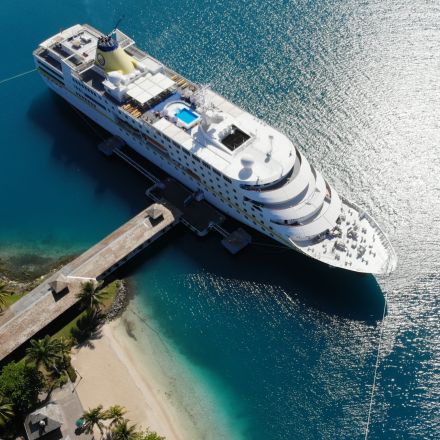Luftaufnahme des Kreuzfahrtschiffs MS Hamburg an einem tropischen Kai mit Steg und türkisblauem Wasser
