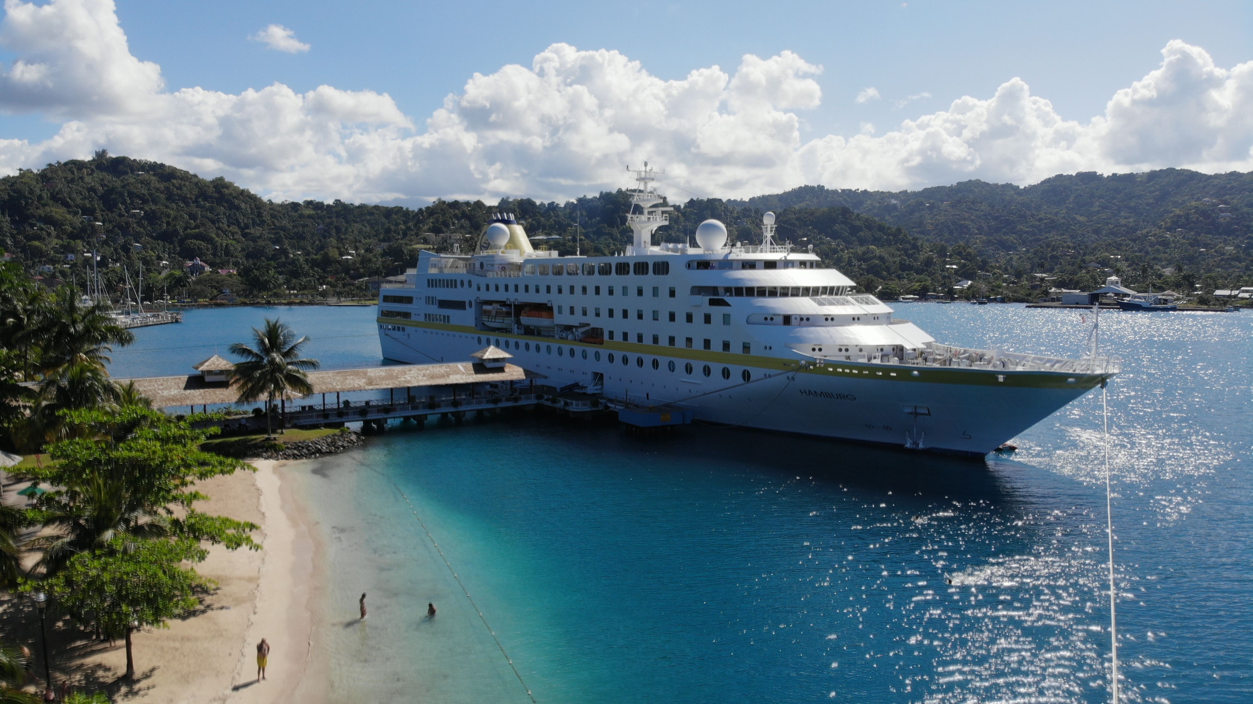 MS Hamburg Kreuzfahrtschiff von Plantours im Karibikhafen mit Strand, Palmen und türkisfarbenem Wasser